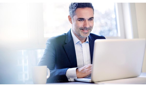 A smiling businessman working on a laptop, in front of window.