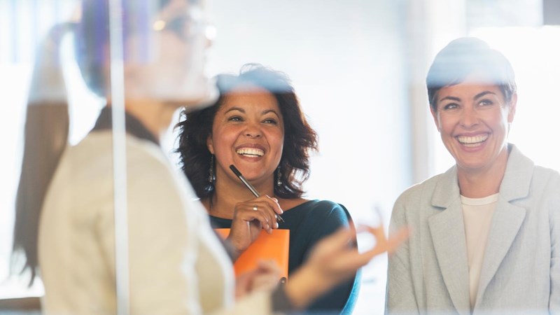 Three businesswomen smiling and talking to each other in an office.
