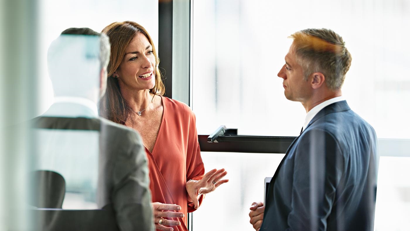 Three business people talking in front of a window.