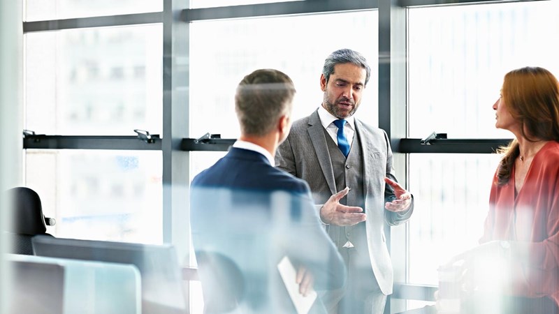 Smartly dressed business people having a discussion next to large windows.