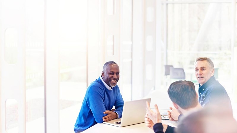 A group of people sitting around a table with laptops during a meeting.
