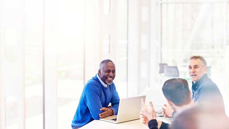 A group of people sitting around a table with laptops during a meeting.