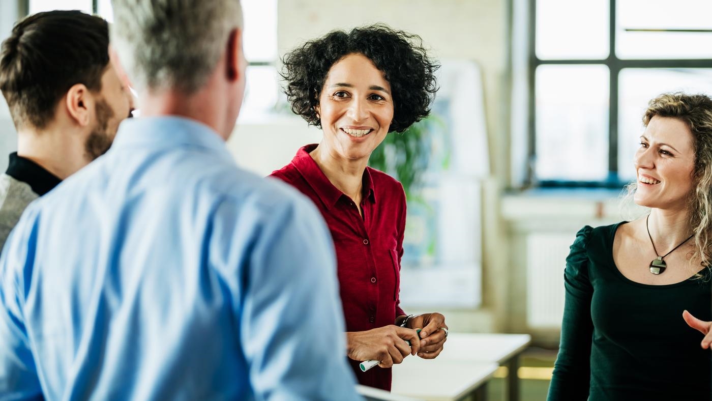 A group of business colleagues standing, having a meeting together in a bright, modern office environment.