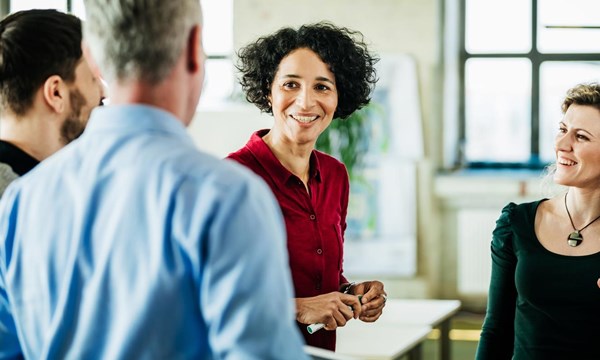 A group of business colleagues standing, having a meeting together in a bright, modern office environment.