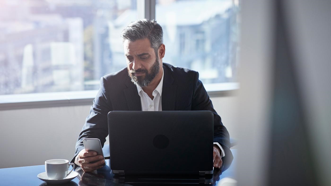 Modern chic business people working in an incredible modern & original office space. A man uses his smartphone and laptop.