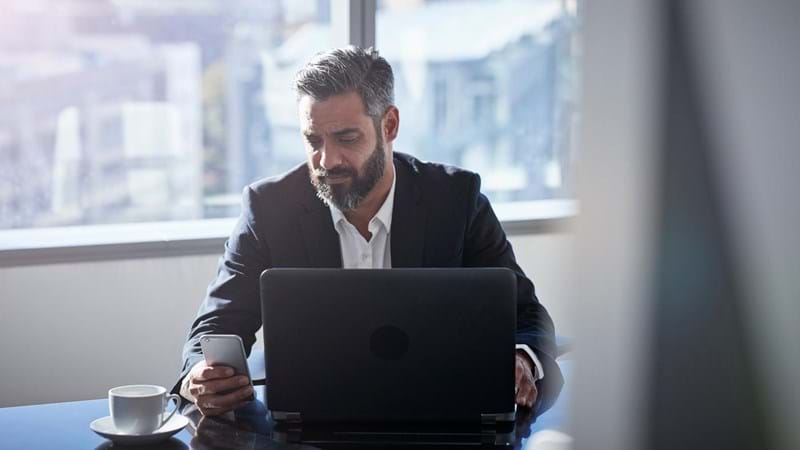 Modern chic business people working in an incredible modern & original office space. A man uses his smartphone and laptop.