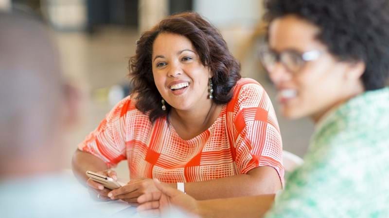 Design professionals discussing project in creative office, one lady is smiling and holding a smartphone.
