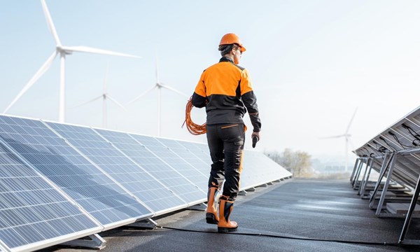 A worker standing on a roof next solar panels and wind turbines.