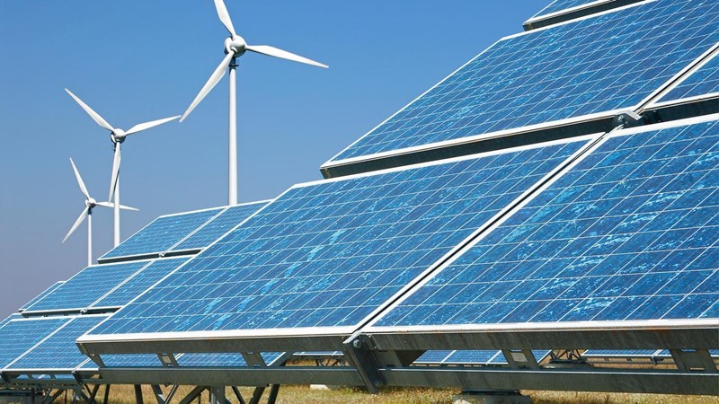 Solar panels and wind turbines in a field, against a clear blue sky.