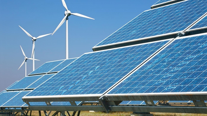 Solar panels and wind turbines in a field, against a clear blue sky.