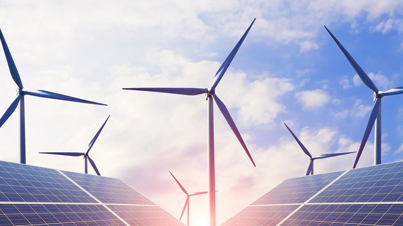 Solar panels and wind turbines against a blue sky at sunset.