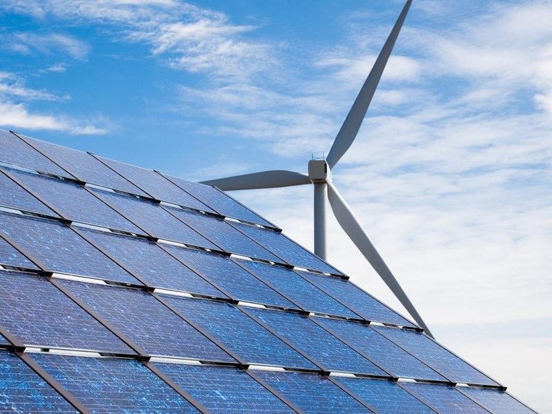 Solar panels and a wind turbine against a blue sky.