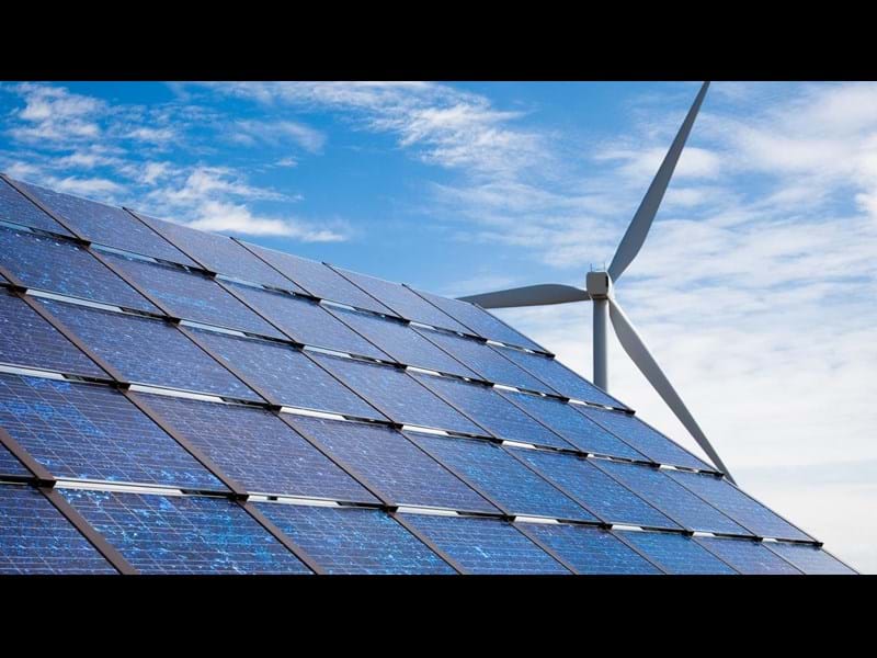 Solar panels and a wind turbine against a blue sky.