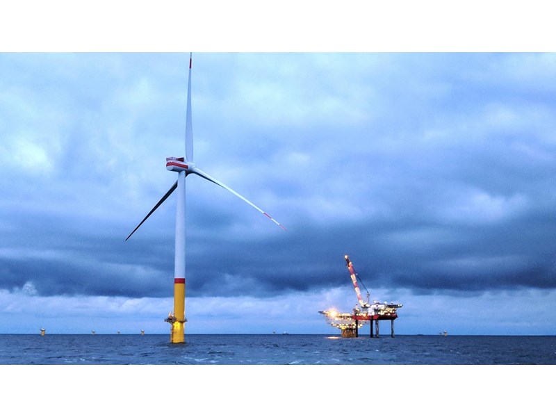 A wind turbine and oil rig in the ocean with a cloudy sky.