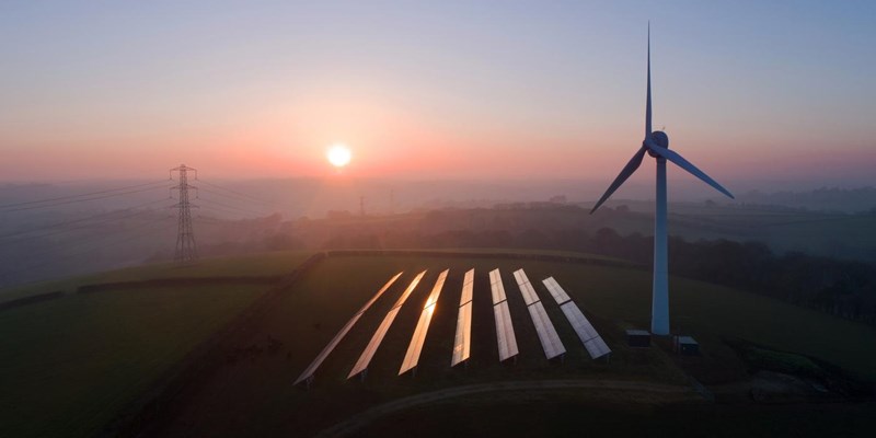 An aerial view of solar panels and a wind turbine in a field at sunset.