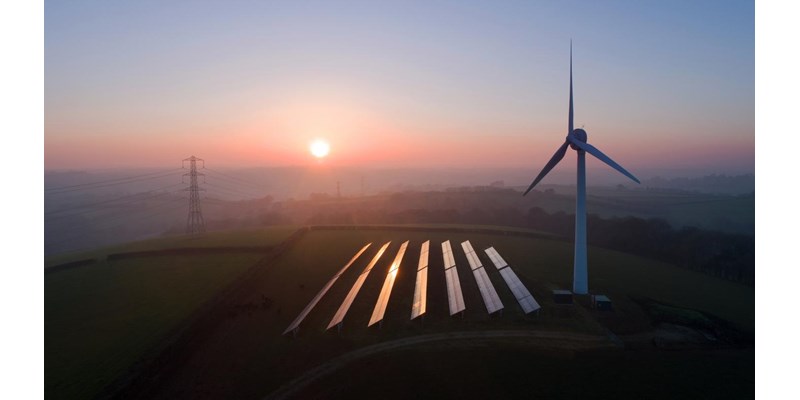 An aerial view of solar panels and a wind turbine in a field at sunset.