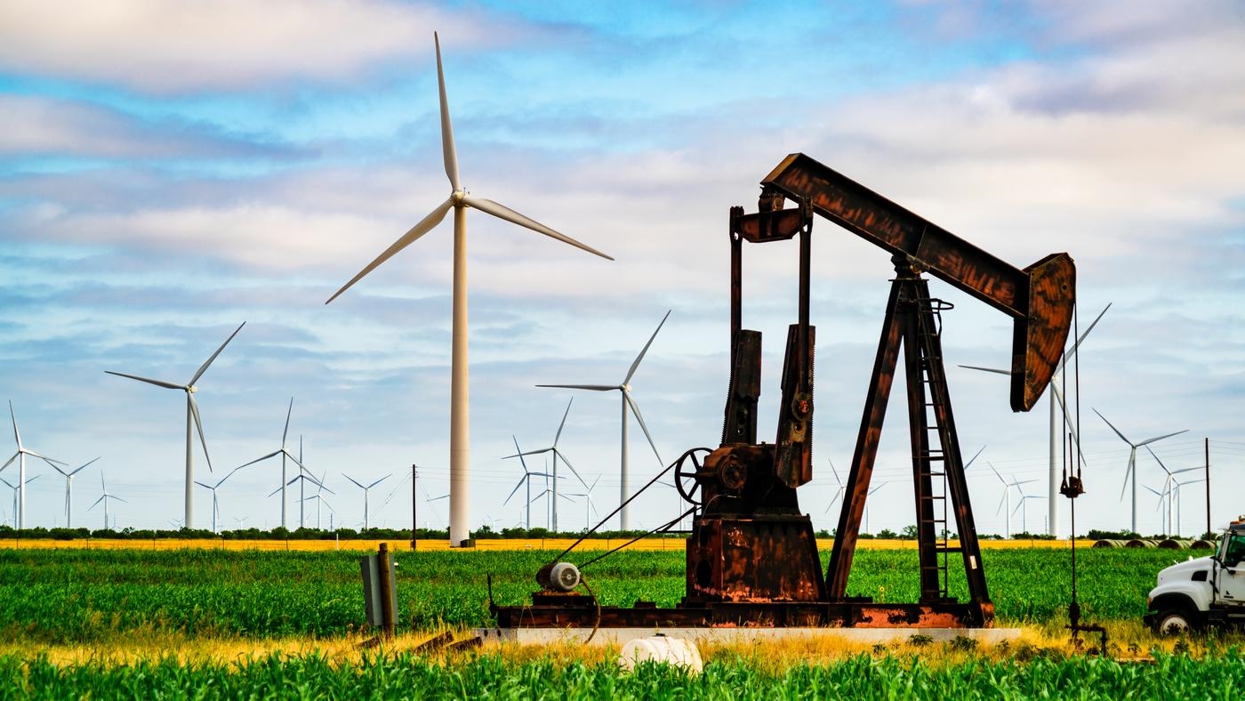 An oil well and wind turbines in a field.
