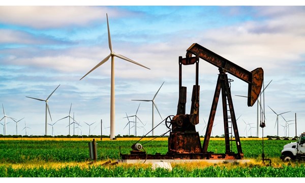 An oil well and wind turbines in a field.