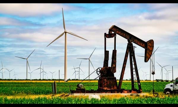 An oil well and wind turbines in a field.