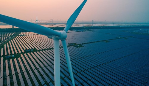 An aerial view of a wind turbine and countless rows of solar panels.