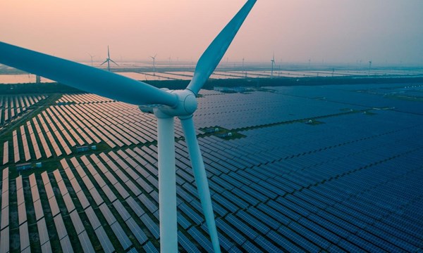 An aerial view of a wind turbine and countless rows of solar panels.
