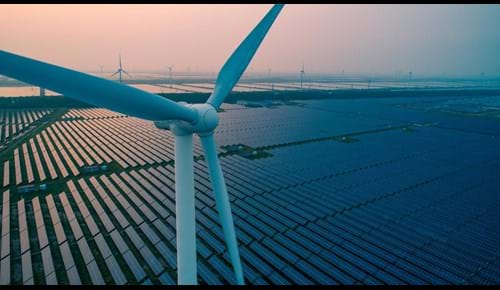 An aerial view of a wind turbine and countless rows of solar panels.
