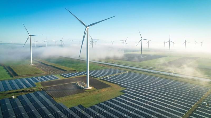 An aerial view of wind turbines and solar panels, in mist countryside fields.