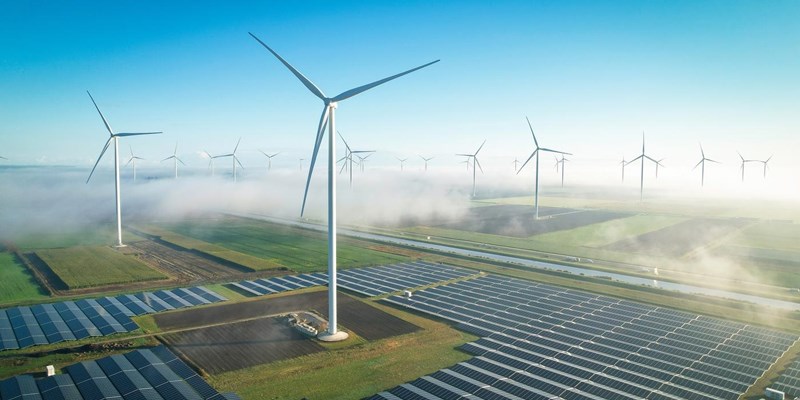 An aerial view of wind turbines and solar panels, in mist countryside fields.