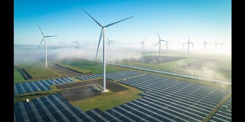 An aerial view of wind turbines and solar panels, in mist countryside fields.