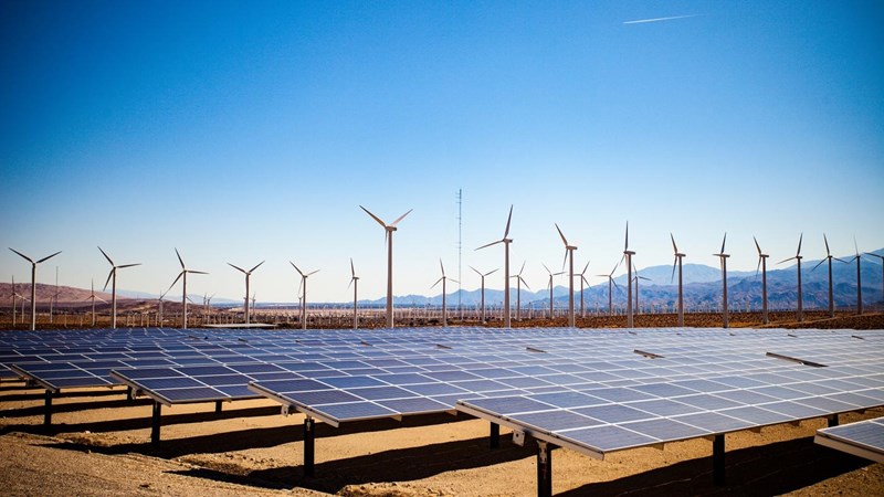 Solar panels and wind turbines in the desert on a backdrop of mountains and clear blue skies.