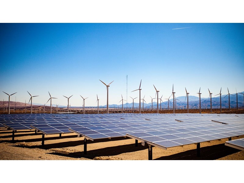 Solar panels and wind turbines in the desert on a backdrop of mountains and clear blue skies.