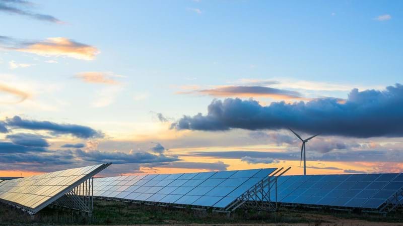 Solar panels in a field during a partially cloudy sunset.