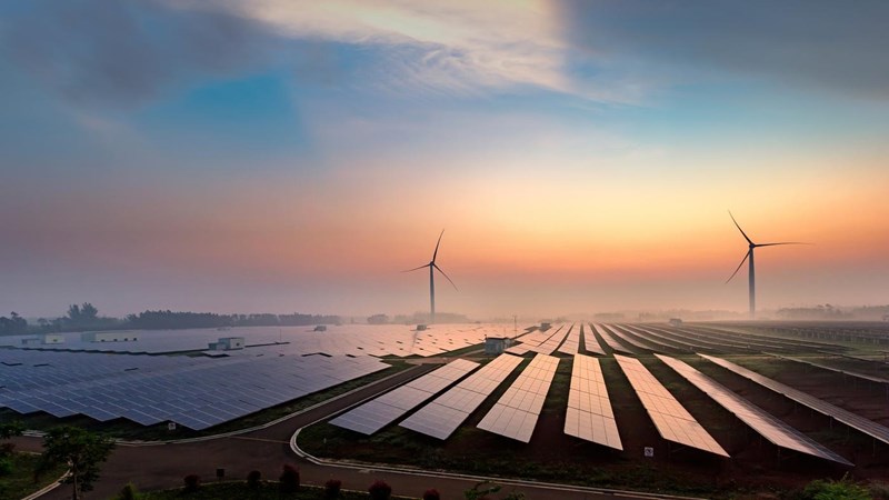 Solar panels and wind turbines across country fields at sunset.