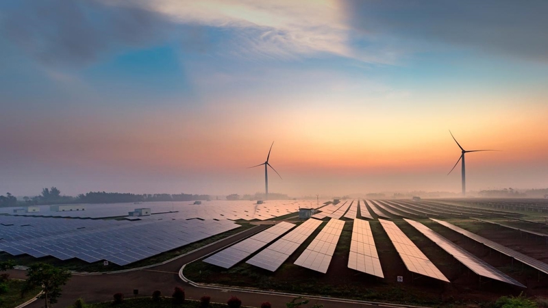 Solar panels and wind turbines across country fields at sunset.