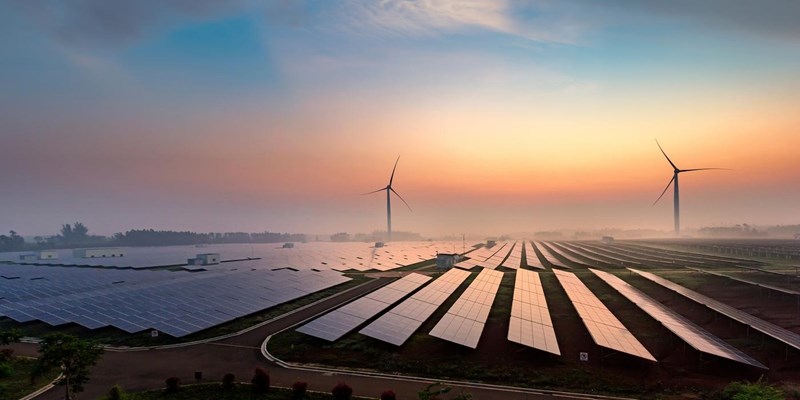 Solar panels and wind turbines across country fields at sunset.