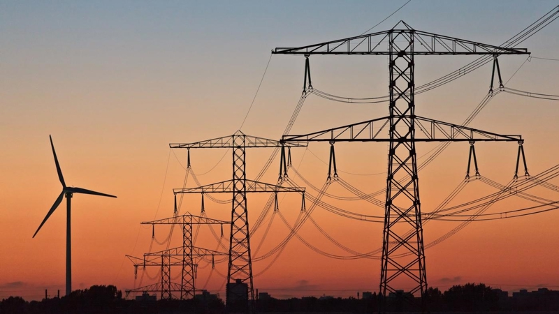 Wind turbines and electricity pylons at sunset.