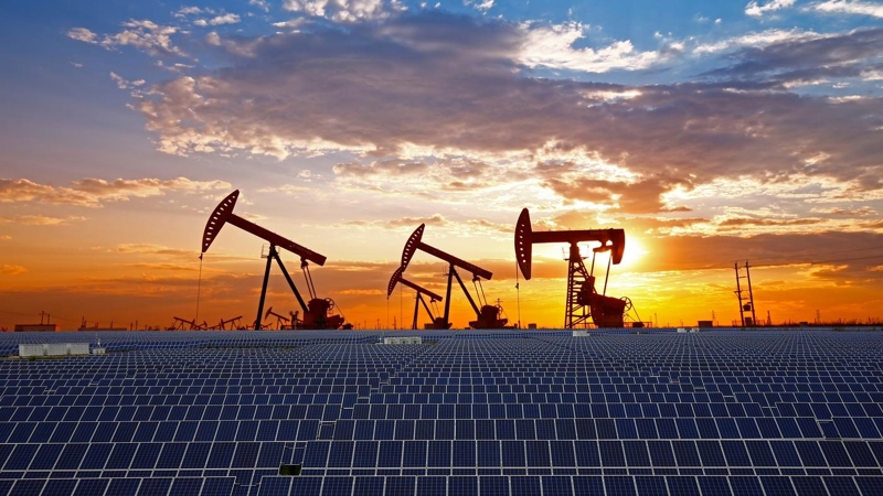 Oil pumps and countless rows of solar panels at sunset.