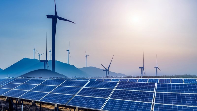 Solar panels and wind turbines in a field., surrounded by hills at dusk.