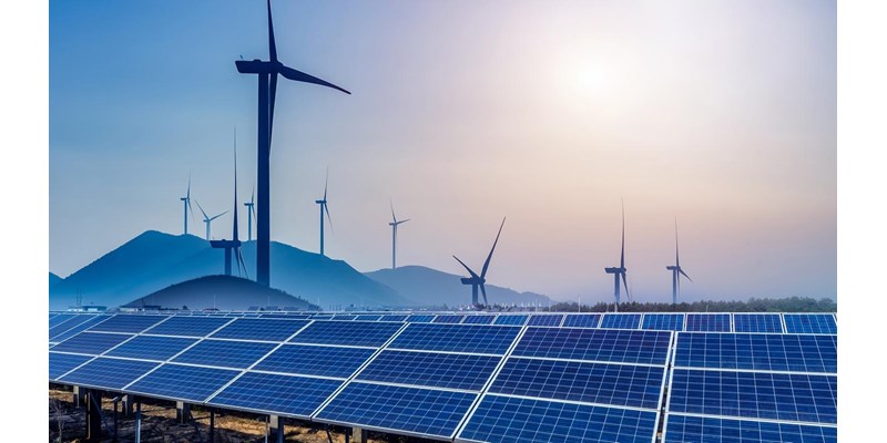 Solar panels and wind turbines in a field., surrounded by hills at dusk.