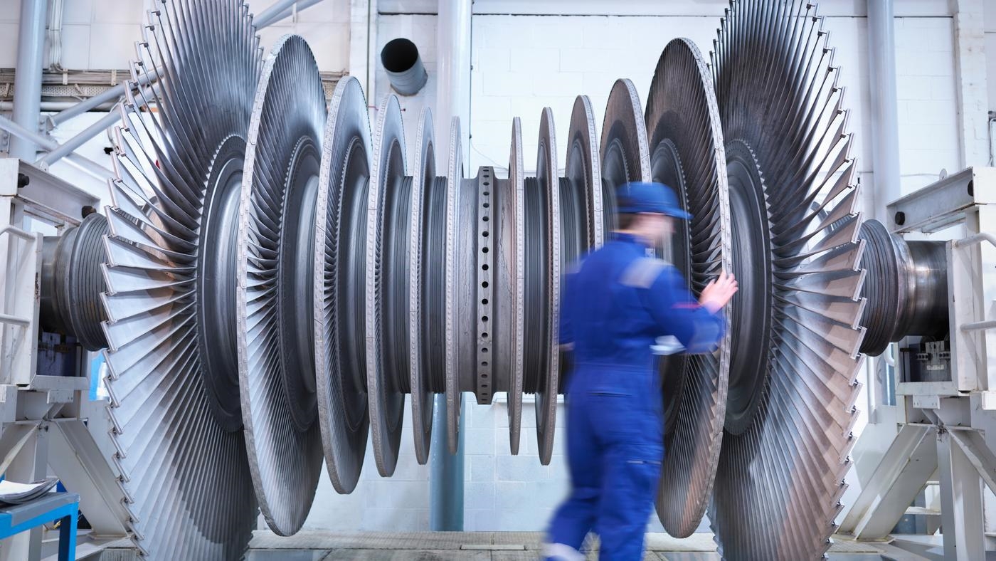 A worker standing next to a large turbine in a factory.