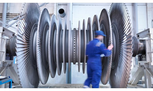 A worker standing next to a large turbine in a factory.