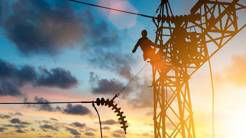 Two men are working on a high voltage power line at sunset.