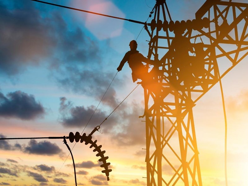 Two men are working on a high voltage power line at sunset.