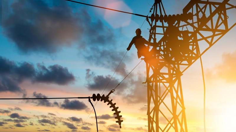 Two men are working on a high voltage power line at sunset.