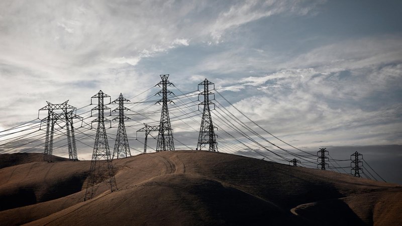 A group of electricity pylons on rolling countryside hills at dusk.