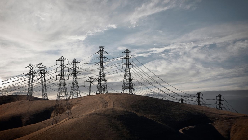 A group of electricity pylons on rolling countryside hills at dusk.