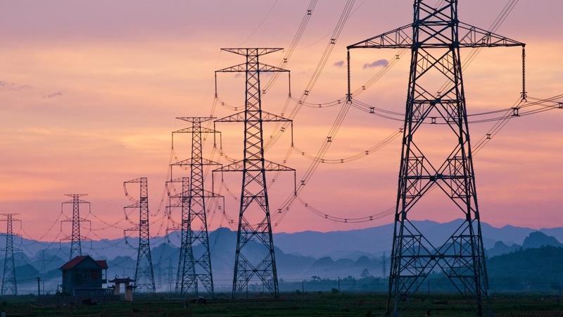 Electricity pylons at sunset, mountains are visible on the horizon.