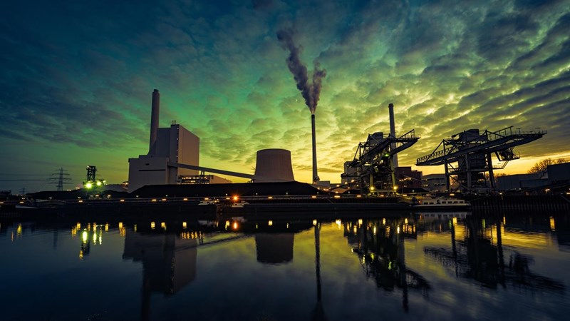 A energy refinery is reflected in a body of water, against an ominous looking green sky.