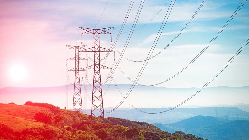 High voltage pylons on a hillside at sunset.