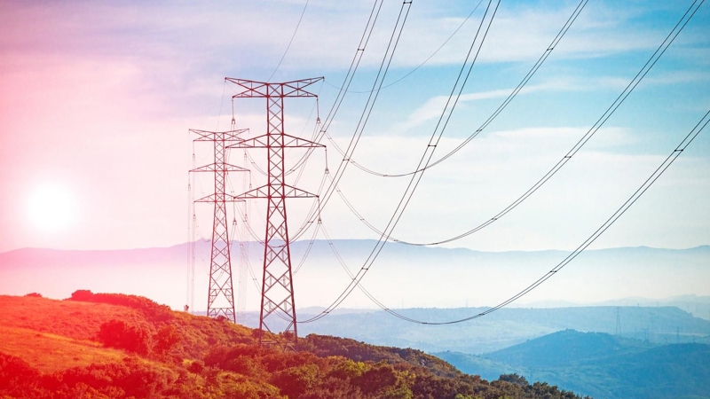 High voltage pylons on a hillside at sunset.